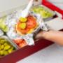A close-up photo of a person putting pickles on their cheeseburger in front of a Five Guys catering box of toppings. A close-up photo of a person putting pickles on their cheeseburger in front of a Five Guys catering box of toppings.