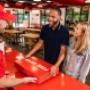A couple collect their Five Guys catering box from a Five Guys employee at a Five Guys restaurant. A couple collect their Five Guys catering box from a Five Guys employee at a Five Guys restaurant.