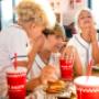 Children chat and laugh while enjoying their Five Guys meals at a dining room table in a Five Guys restaurant. Children chat and laugh while enjoying their Five Guys meals at a dining room table in a Five Guys restaurant.