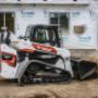 Bobcat Construction Equipment Compact Truck Loader with Bucket Attachment plowing dirt at construction site for a new building. Bobcat Construction Equipment Compact Truck Loader with Bucket Attachment plowing dirt at construction site for a new building.