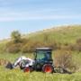 Bobcat construction tractor with three-point finish mower driving through hilly countryside. Bobcat construction tractor with three-point finish mower driving through hilly countryside.