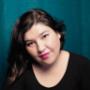 Paula, the owner of Precious Paws Photography, is shown in a softly lit headshot. She has shoulder-length dark hair, natural makeup with bright pink lipstick, and wears a simple black top. Set against a teal backdrop Paula, the owner of Precious Paws Photography, is shown in a softly lit headshot. She has shoulder-length dark hair, natural makeup with bright pink lipstick, and wears a simple black top. Set against a teal backdrop