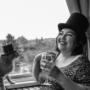 Whimsical black-and-white image of a woman in a patterned dress and top hat smiling while toasting with a cat, who is also wearing a top hat. Set against a rainy window view, this playful scene combines humor and charm. Whimsical black-and-white image of a woman in a patterned dress and top hat smiling while toasting with a cat, who is also wearing a top hat. Set against a rainy window view, this playful scene combines humor and charm.