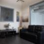 Cozy waiting area with a black leather couch, neutral-toned decor, and a small entertainment stand. Art on the walls and soft lighting create a welcoming ambiance. Cozy waiting area with a black leather couch, neutral-toned decor, and a small entertainment stand. Art on the walls and soft lighting create a welcoming ambiance.