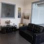 Cozy waiting area with a black leather couch, neutral-toned decor, and a small entertainment stand. Art on the walls and soft lighting create a welcoming ambiance. Cozy waiting area with a black leather couch, neutral-toned decor, and a small entertainment stand. Art on the walls and soft lighting create a welcoming ambiance.