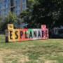 A colourful and textured sign reads "The Esplanade" on a grassy field. A colourful and textured sign reads "The Esplanade" on a grassy field.